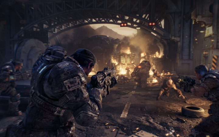 COG soldiers take cover and fire at Locust forces under a burning bridge in Gears of War: E-Day
